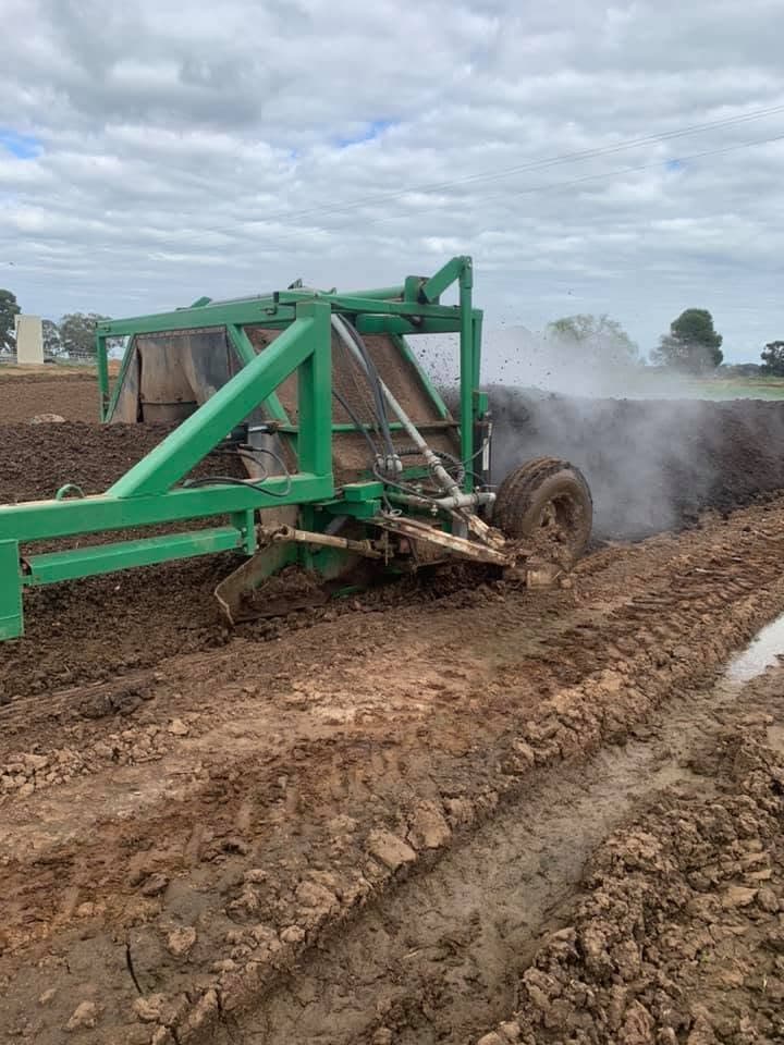 Compost turner working a windrow with steam rising