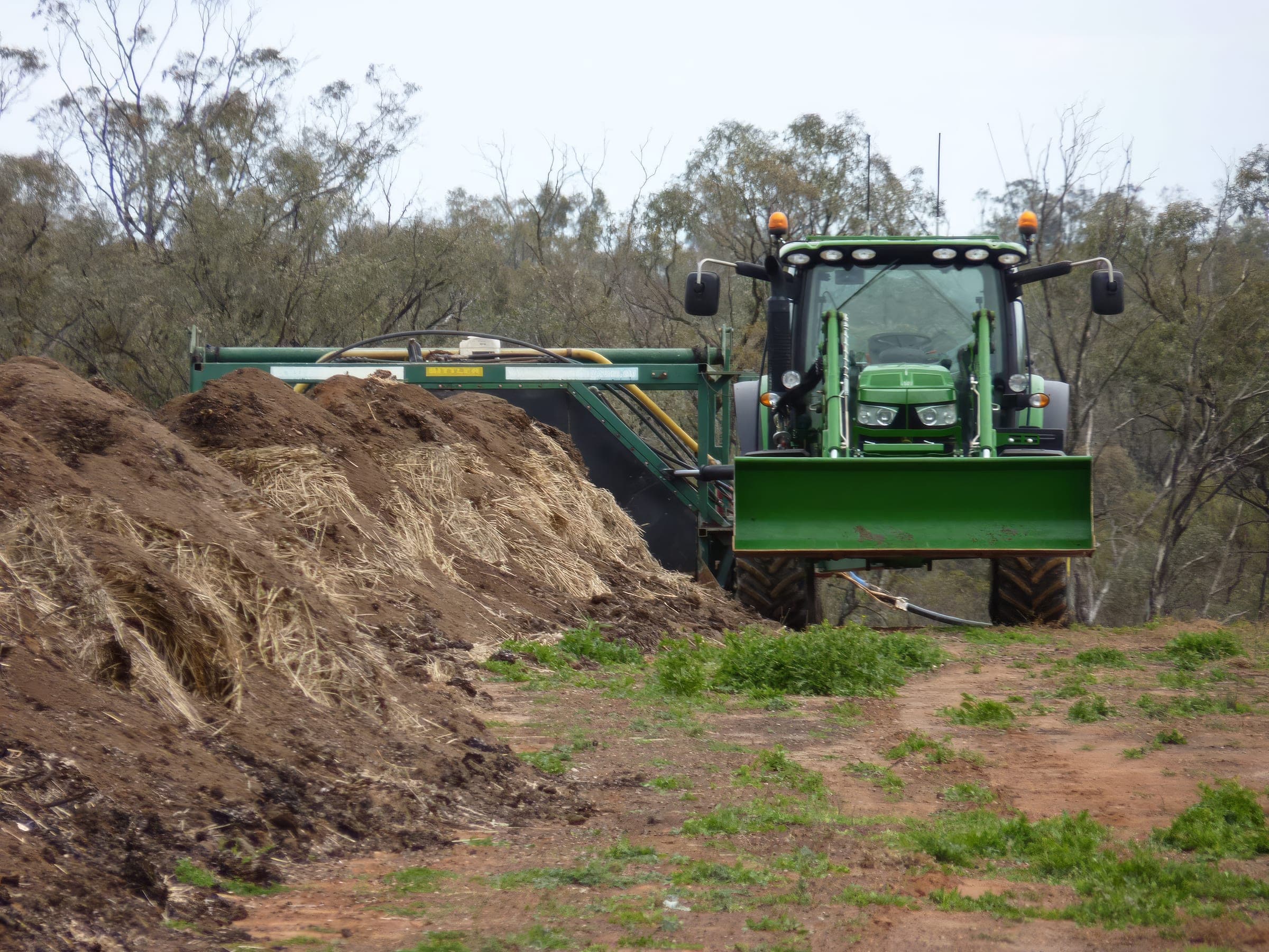 Green tractor with compost turner working a windrow of organic material