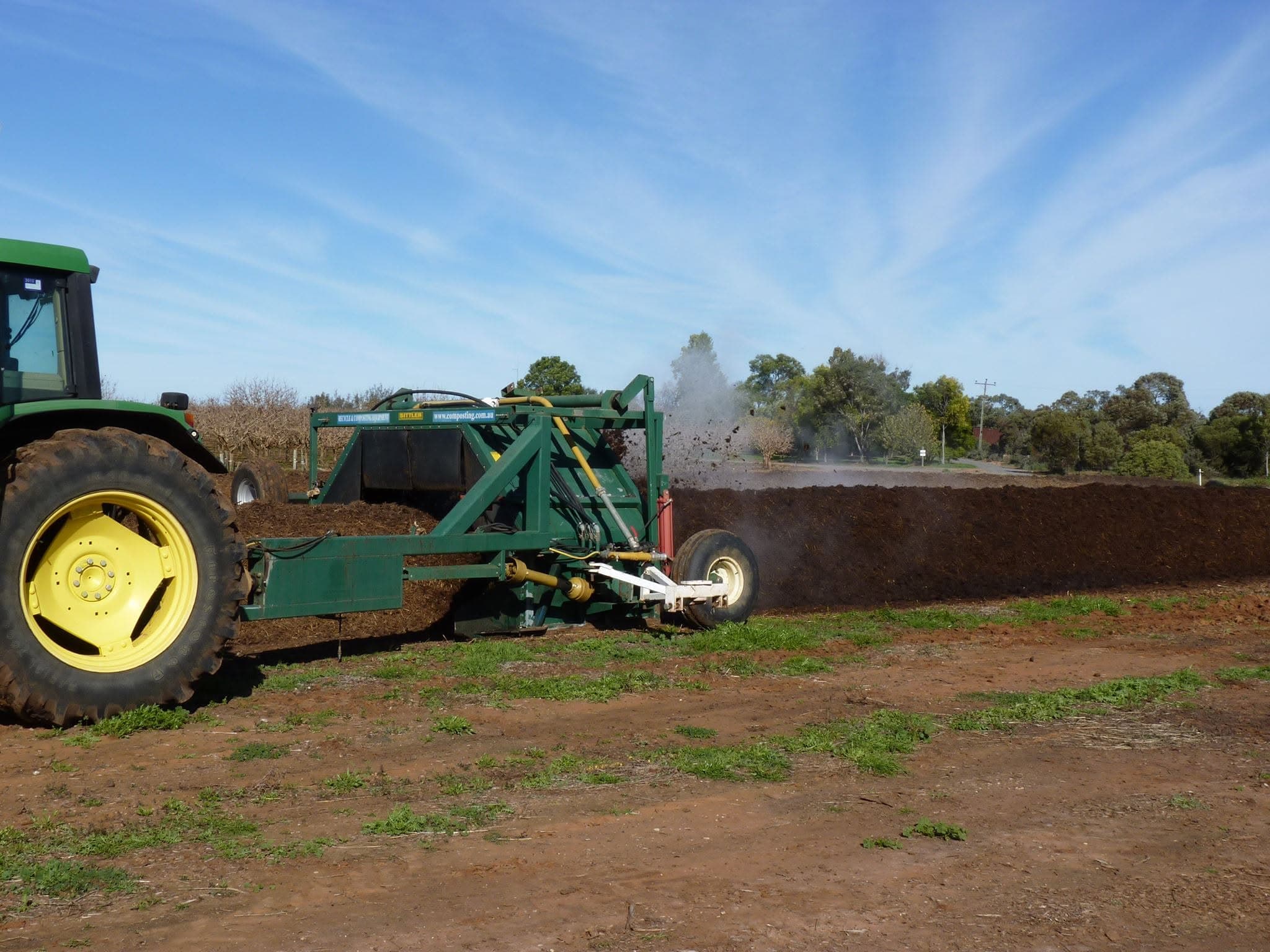 Tractor towing a compost turner throwing material as it turns a windrow