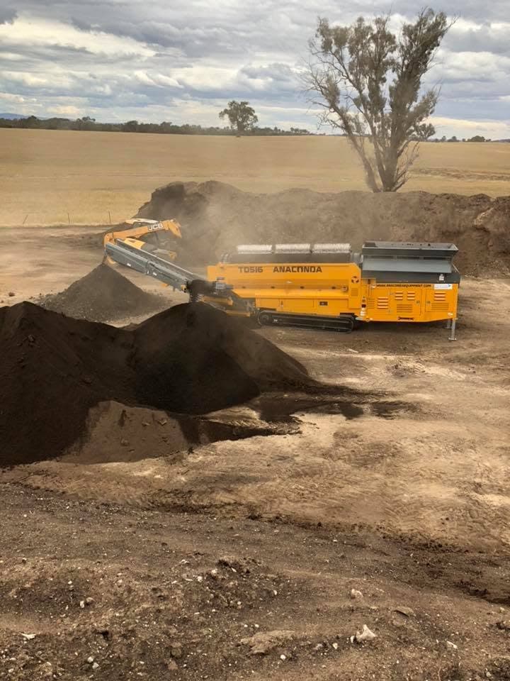 Excavator loading a mobile screening machine processing compost