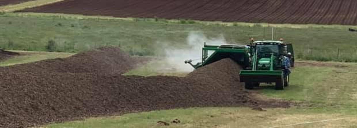 Tractor turning a compost windrow with hills and paddocks in the background